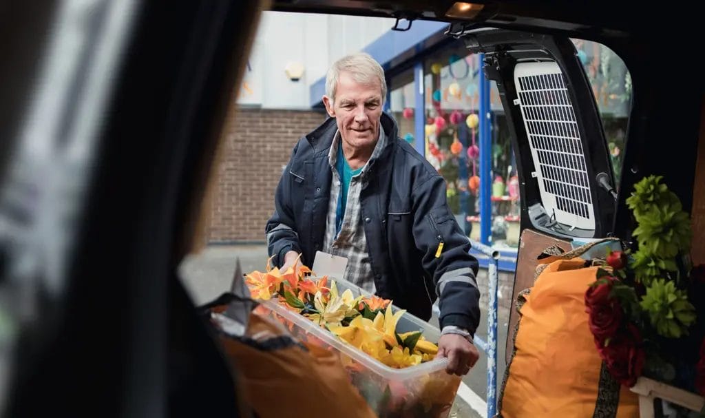 A businessman loads fake florals, amongst other event decor, into the back of a work van to transport to an event.