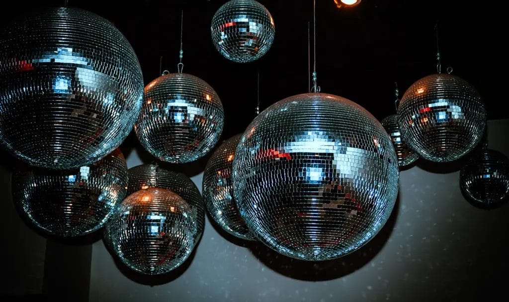 A flash photo of various sized disco balls hanging from the ceiling as party decor.