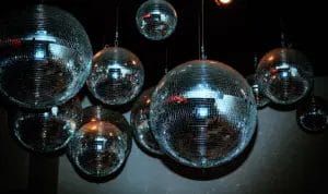 A flash photo of various sized disco balls hanging from the ceiling as party decor.