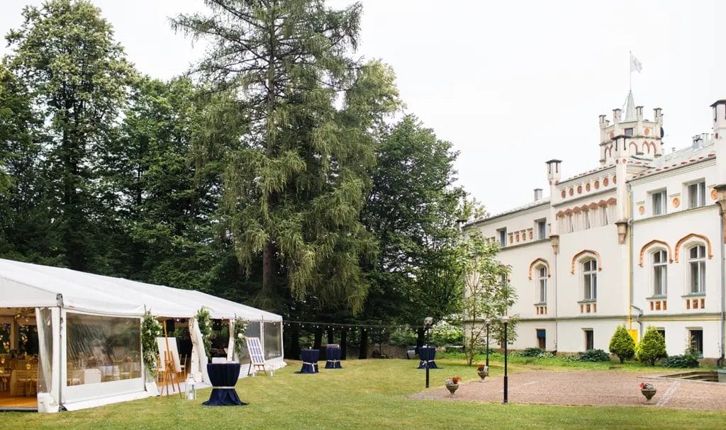 A large, outdoor event tent is set up on the lawn of a private estate for an event.