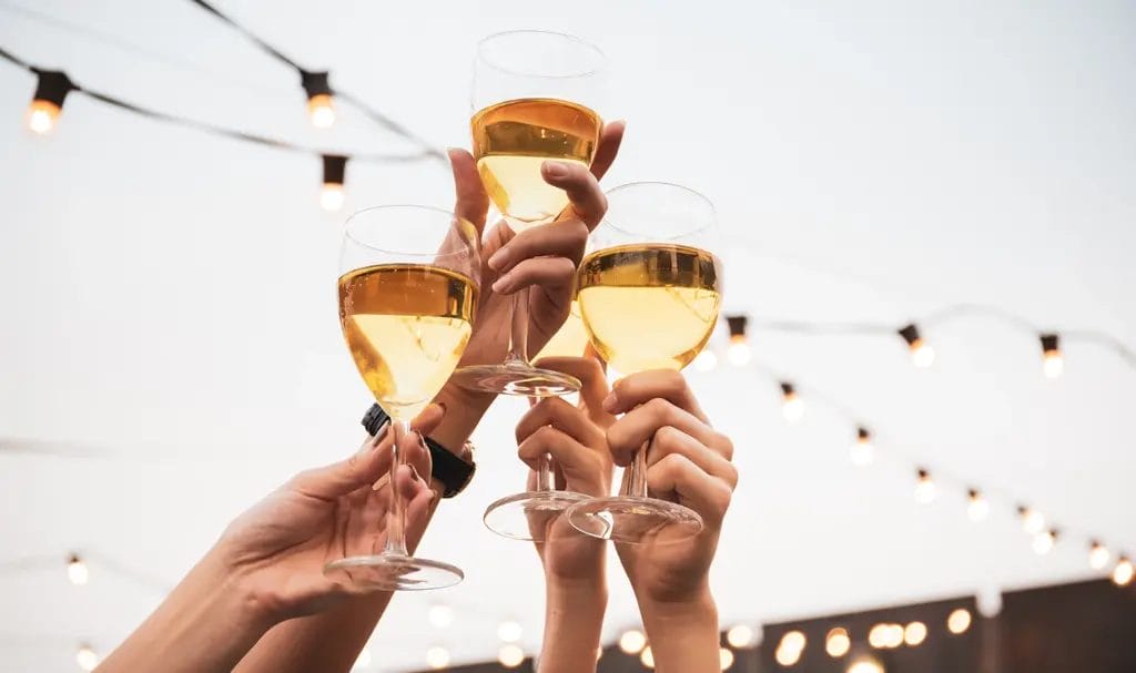 A set of four hands raise champagne flutes in the air to cheers and toast to a celebration.