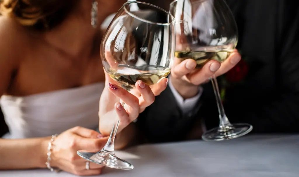A bride and groom clink wine glasses as they share a moment together on their wedding day.
