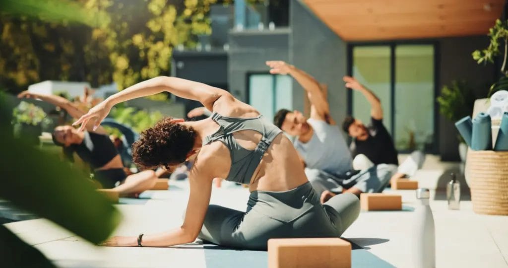 Back view of a yoga teacher facing her outdoor patio class, performing a side bend.