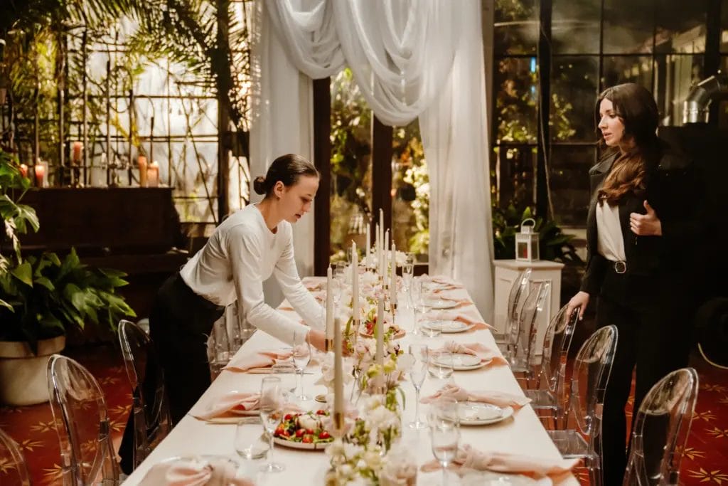 Event planner supervises decorator while setting table in event hall.