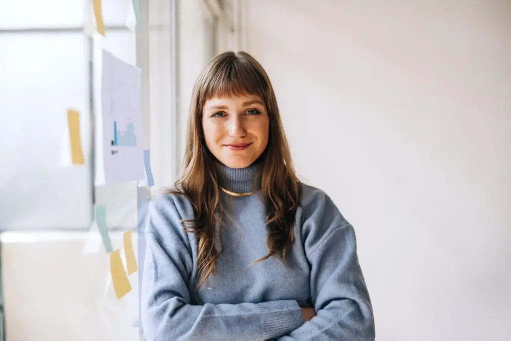 Portrait of a life coach looking at the camera while leaning on a glass idea board filled with post-its.