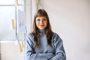 Portrait of a life coach looking at the camera while leaning on a glass idea board filled with post-its.