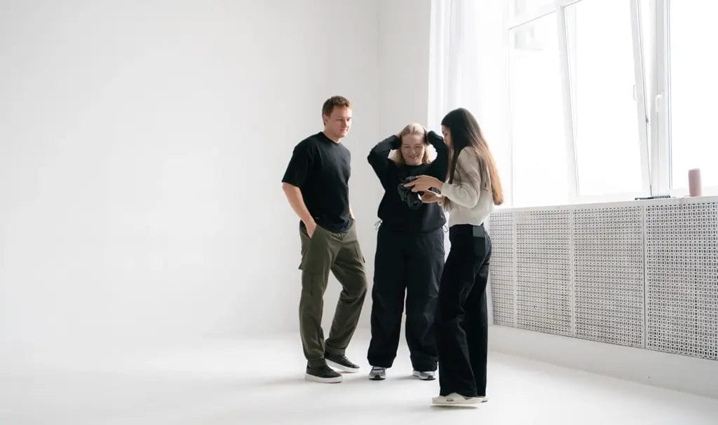A photographer shows a couple the photos on her camera as they stand in a white studio space.