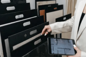 Close-up of an interior designer comparing flooring samples while looking at a floor plan on her tablet.