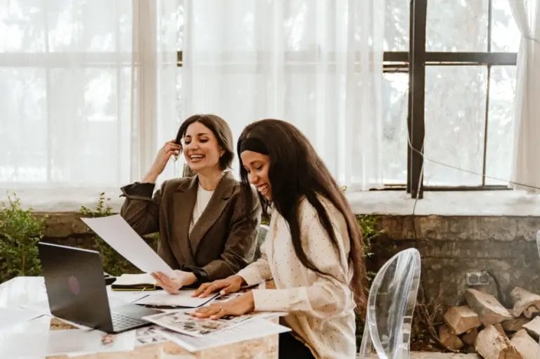 two women laughing while sorting through paperwork at an event venue