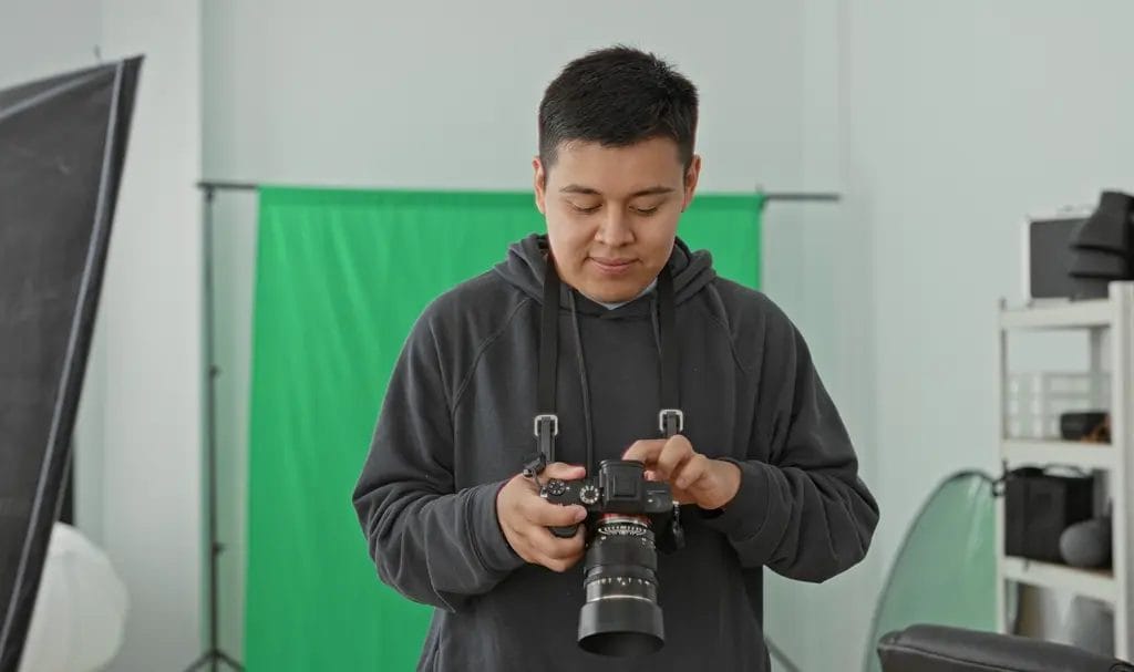 Photographer softly smiles as he looks through the recent shots on his camera in his home studio.